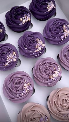 twelve cupcakes with purple icing and pearls on them are arranged in a box