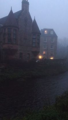 an old building is next to a river in the fog