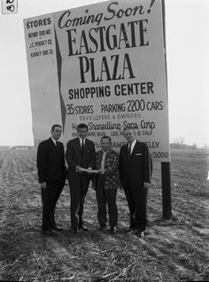 black and white photograph of three men standing in front of an eastgate plaza sign