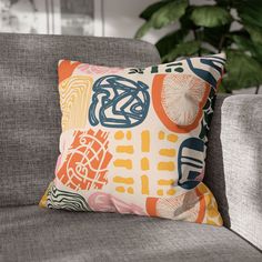 an orange and blue pillow sitting on top of a gray couch next to a potted plant