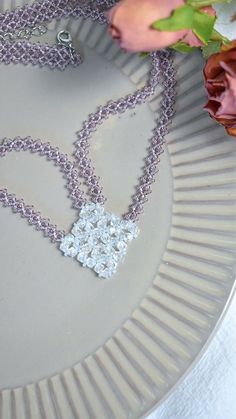 a close up of a necklace on a plate with flowers in the backgroud