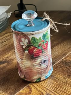 a canister with strawberries painted on it sitting on a wooden table next to plates