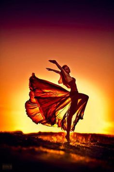 a woman is dancing in the sunset with her arms spread out and legs bent forward