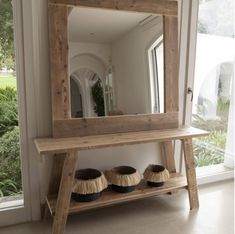 a mirror and some baskets on a wooden shelf in front of a window with plants