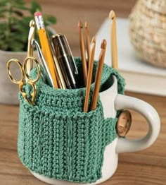 a cup filled with pens and pencils sitting on top of a wooden table next to a potted plant