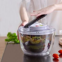 a person cutting vegetables in a food processor on a table with tomatoes and lettuce