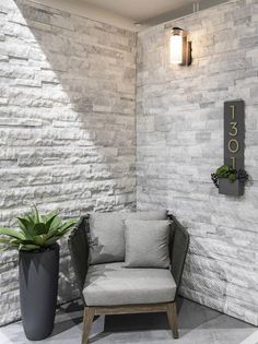 a chair sitting in front of a white brick wall next to a potted plant