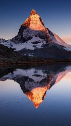 a mountain is reflected in the still water at sunset, with its reflection on the lake's surface