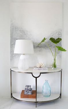 a table with two vases on it and a lamp next to it in front of a painting