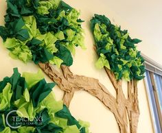 two paper trees are hanging on the wall in front of a window, with one tree made out of green tissue paper