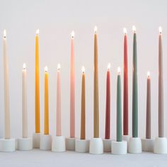 seven candles lined up in different colors on a white surface with no one around them