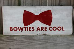 a sign that says bowties are cool on the side of a wooden fence with a red bow tie