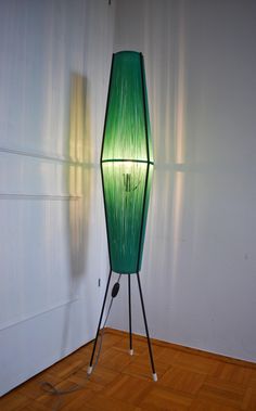 a green floor lamp sitting on top of a hard wood floor next to a white wall