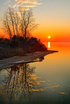 the sun is setting over some water and trees