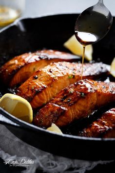 a pan filled with salmon being drizzled with lemons and seasoning