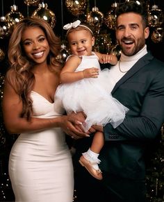 a man and woman holding a baby in front of a christmas tree with baubs