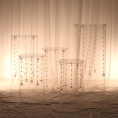 three clear vases sitting on top of a bed next to a sheered curtain