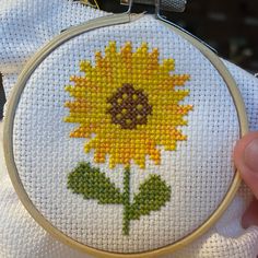 a cross stitch sunflower is being held by someone's hand while they are holding it