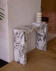 a marbled console table sitting next to a brick wall in a room with hardwood floors