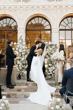 a bride and groom kissing in front of their wedding ceremony arch with white flowers on it