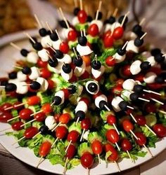 an arrangement of skewered tomatoes and black olives arranged on a white plate