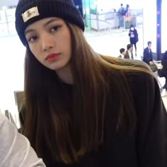 a girl with long hair wearing a beanie and looking at the camera while waiting in an airport