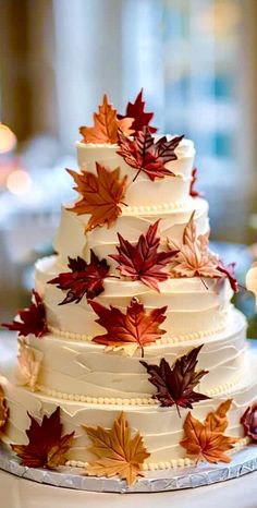 a wedding cake decorated with fall leaves on a table in front of candles and flowers