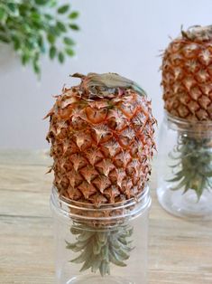 two pineapples sitting in glass jars on a table