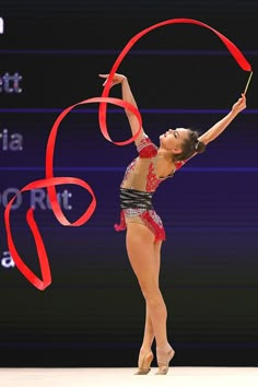 a woman in a red and black leotard doing a trick with a ribbon