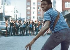 a man riding a skateboard down a street next to a group of people on the sidewalk