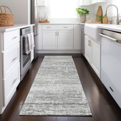 a kitchen with white cabinets and wooden floors, along with a rug on the floor