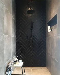 a bathroom with a tiled shower stall and black tile walls, along with a stool in the corner