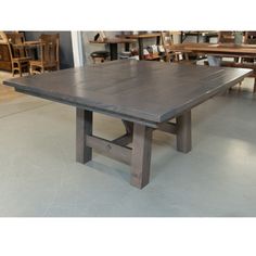 a large wooden table sitting on top of a cement floor next to tables and chairs