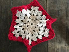 a red and white crocheted dishcloth on a wooden table with a black object in the middle