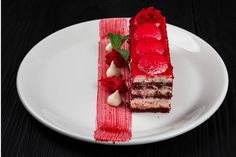 a piece of cake on a white plate with red icing and garnish