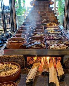 an outdoor grill with many different foods cooking in pots and bowls on the fire pit