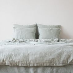 an unmade bed with white linens and two pillows on the headboard, against a pale pink wall