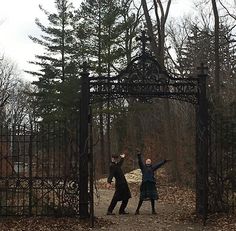 two people standing in front of an iron gate with their arms up and one person reaching for the frisbee