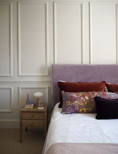 a bed with purple headboard and pillows in a room that has white paneled walls