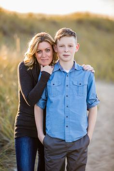 a young man and woman standing next to each other in front of tall grass with the sun shining on them