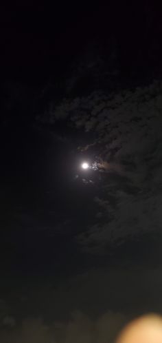 the moon is shining brightly in the dark night sky above some clouds and people are standing on the beach