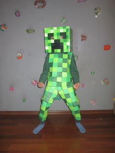 a young boy dressed in a green minecraft costume standing on a hard wood floor