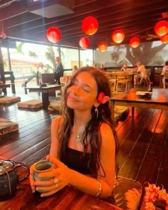 a woman sitting at a table with a cup in her hand and red lanterns hanging from the ceiling