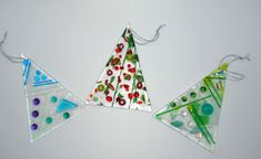 three pieces of glass are hanging from strings on a white surface, each with different designs and colors