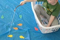 a young boy sitting in a laundry basket holding a fishing rod with fish on it