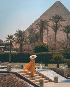 a woman with a straw hat is walking up some steps in front of the pyramids