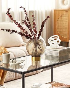 a glass table topped with a vase filled with red flowers next to a white couch