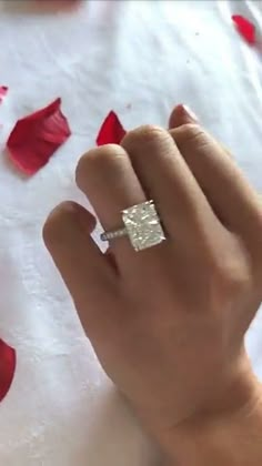 a woman's hand with a ring on it and rose petals scattered around her