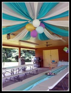 an outdoor party setup with balloons and streamers hanging from the ceiling, tables set up in front of them