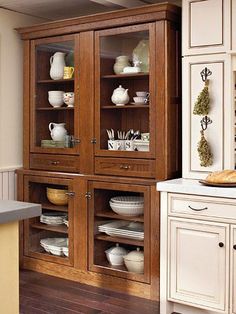 a wooden cabinet with glass doors in a kitchen next to a sink and counter top